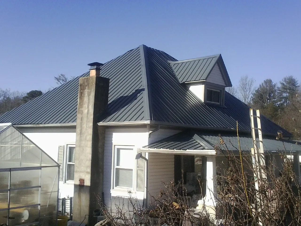 Dark blue standing seam metal roof on a white farmhouse with dormer — Slate & Tile Roof Repair by Roofing Brothers in East Setauket