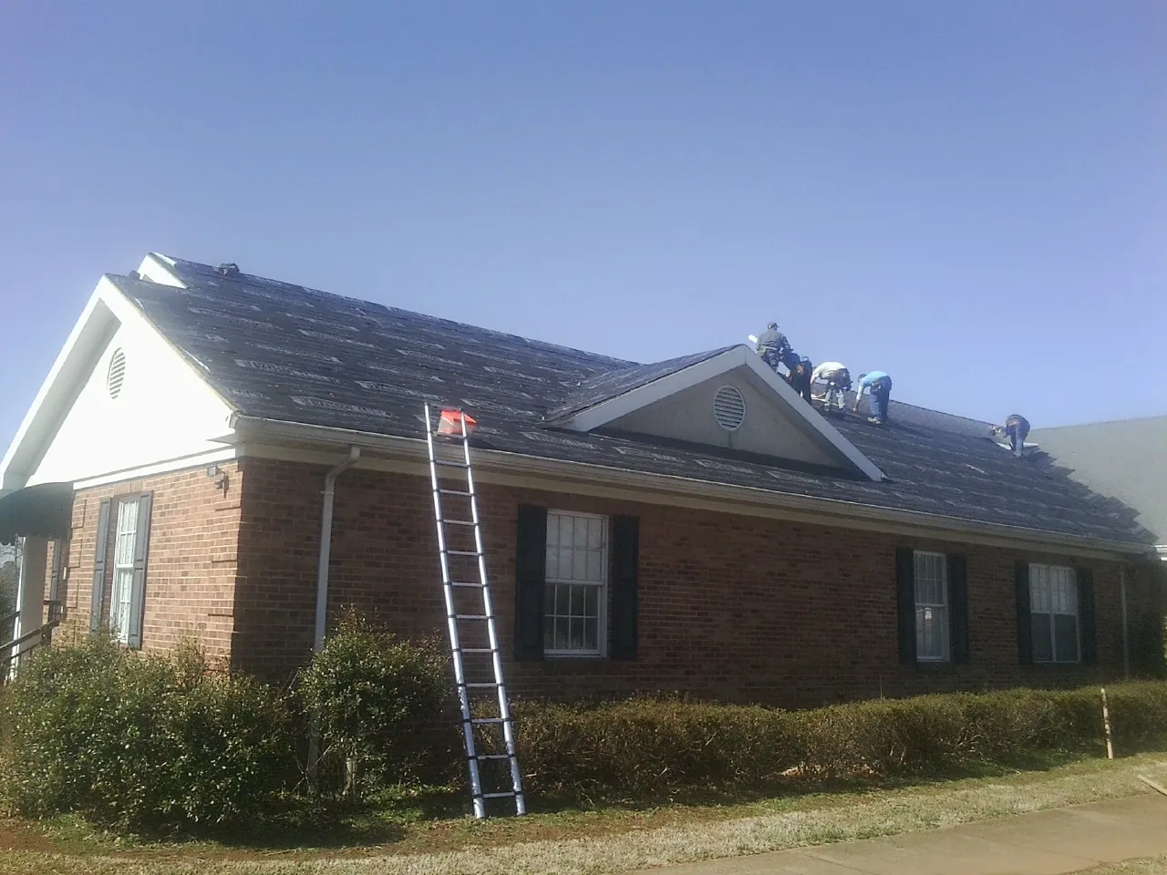 Crew tearing shingles off a brick ranch roof with a ladder set — Metal Roof Repair work by our crew in East Setauket