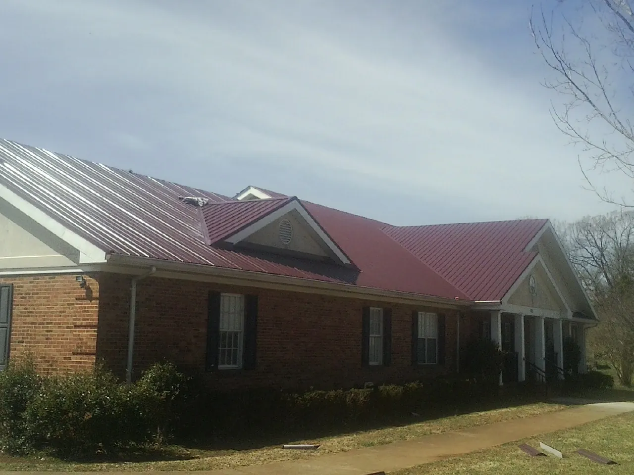 Red metal roof with gabled entries on a long brick building, from a Hail Damage Roof Repair job in East Setauket