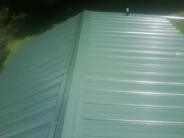 New green metal panels meeting at the ridge of a roof — Flat Roof Repair work by our crew in East Setauket