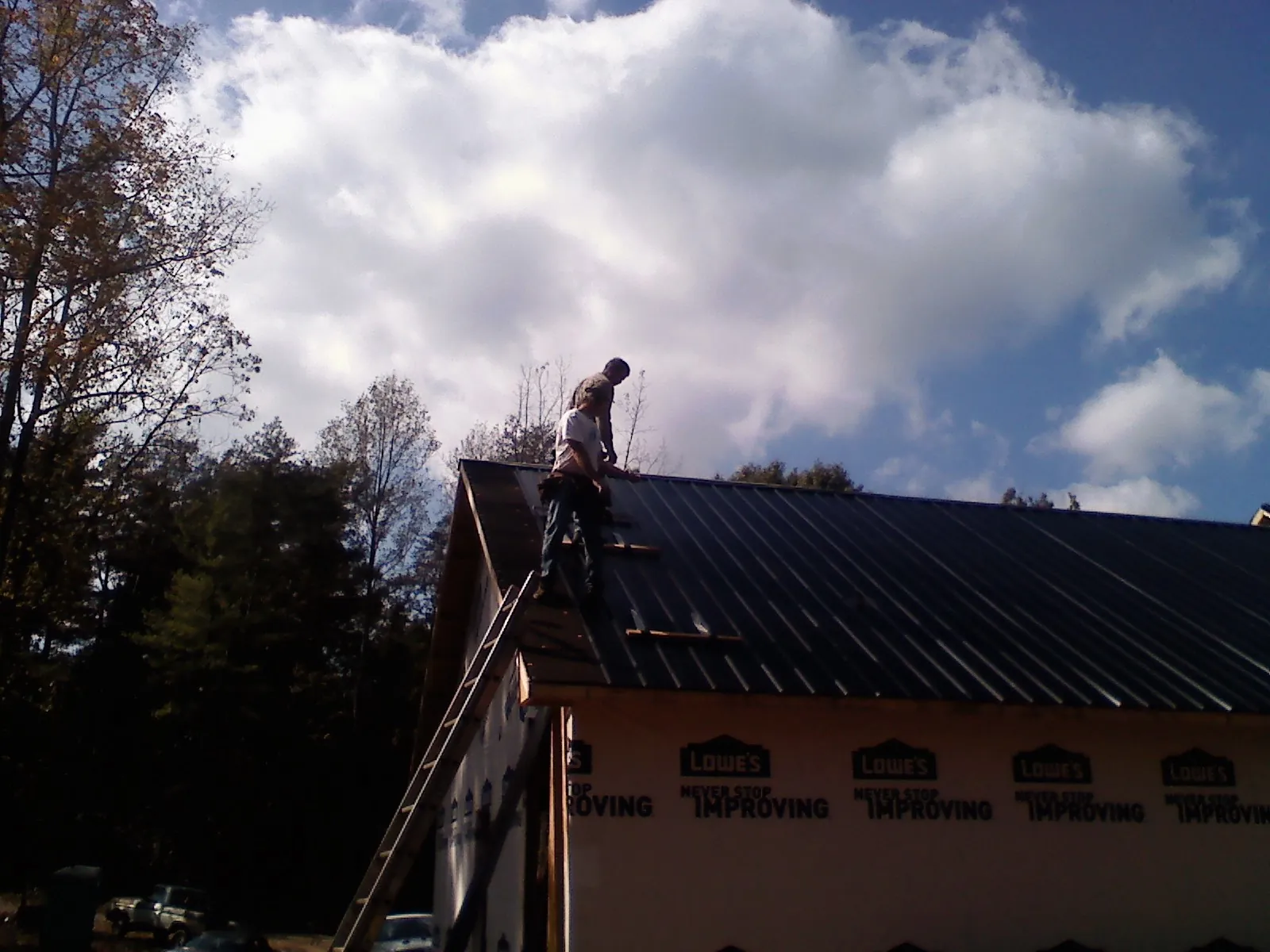 Roofer fastening dark metal panels high against a cloudy sky, from a Roof Inspection job in East Setauket