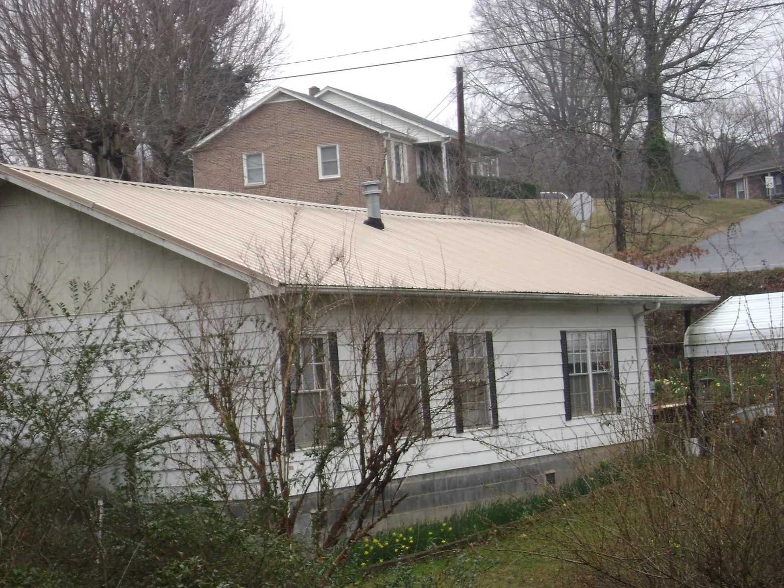 Tan metal roof on a white sided house set into a hillside — Commercial Roofing by Roofing Brothers in East Setauket